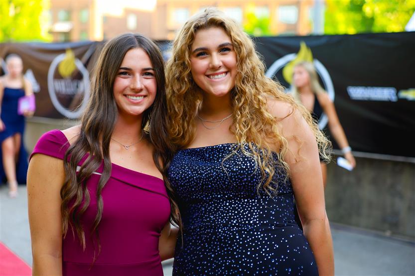 Two young women wearing dresses smile